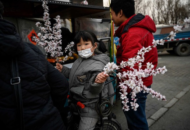 A girl sitting on a bicycle carries peach blossoms in front of a street food stall along a road in Beijing on March 17. China came in first in one poll on happiness, and 64th in a more comprehensive survey. Photo: AFP