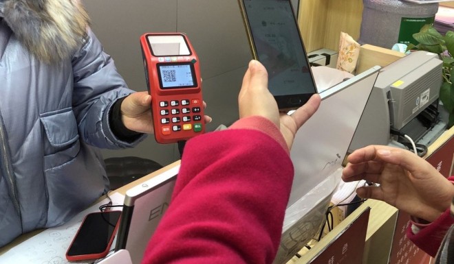 Li Lan, who won a 200-yuan red packet in Suzhou’s e-yuan test, scans a QR code with her smartphone to make a payment at an electronics shop. Photo: Orange Wang