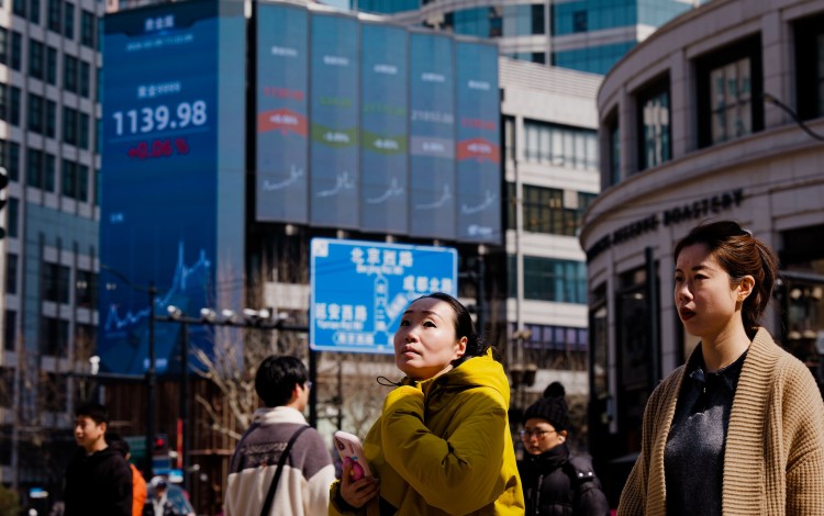 People cross the street beneath a large screen showing the latest stock exchange data in Shanghai. Photo: EPA 