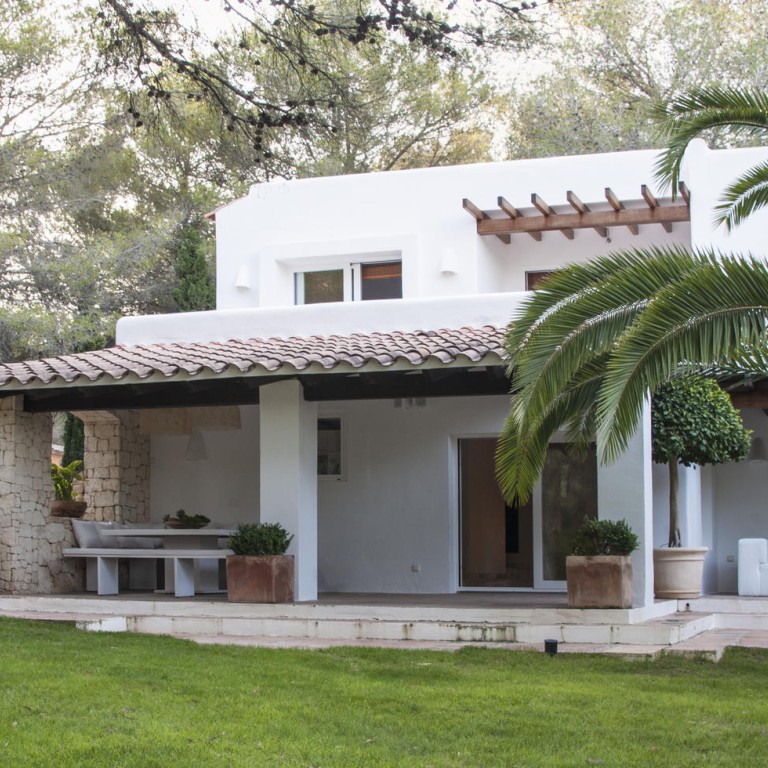 The exterior of the main house with large pine trees and ancient Phoenix palms.