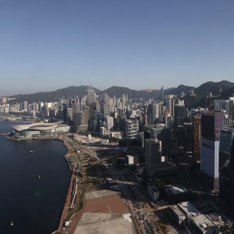An aerial view of a city with skyscrapers and mountains in the background, with a waterfront visible in the foreground.