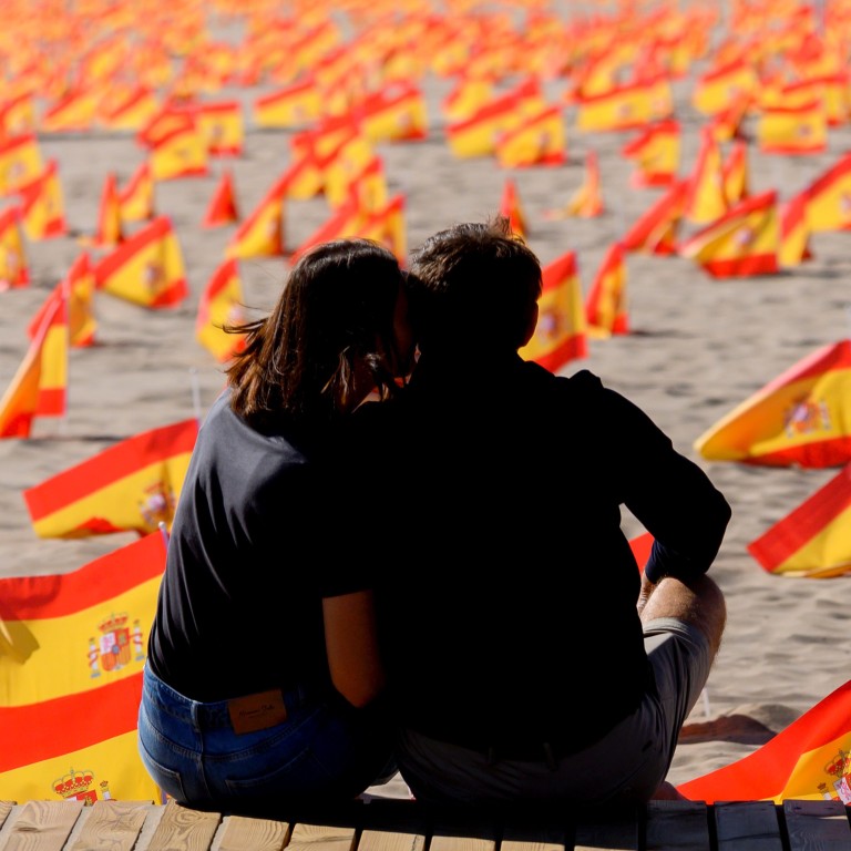 A couple sit next to thousands of Spanish flags, representing the Spanish victims of Covid-19, on Patacona beach in Valencia on October 4. Photo: AFP