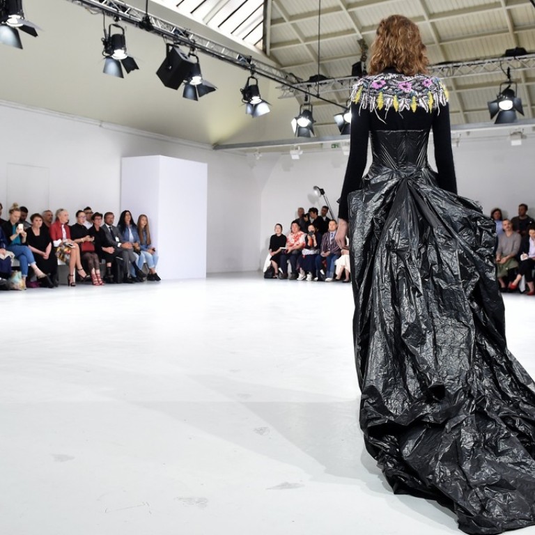 Models wearing a garbage bag dress with a trash can lid hat, a dry