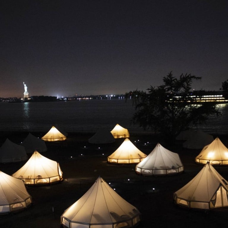 Glowing Journey Tents at night in the foreground with the Statue of Liberty and Staten Island Ferry behind. Photo: David Gray/Bloomberg