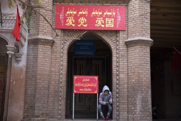 A child rests near the entrance to a mosque where a banner  reads “Love the party, Love the country” in Kashgar in Xinjiang.  Photo: AP 