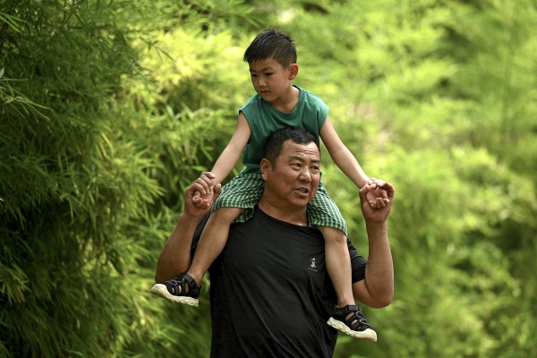 A man carries a child on his shoulders along a street in Beijing on August 2, 2022. Falling births is accelerating population ageing in China, a problem it has grappling with for years. Photo: AFP
