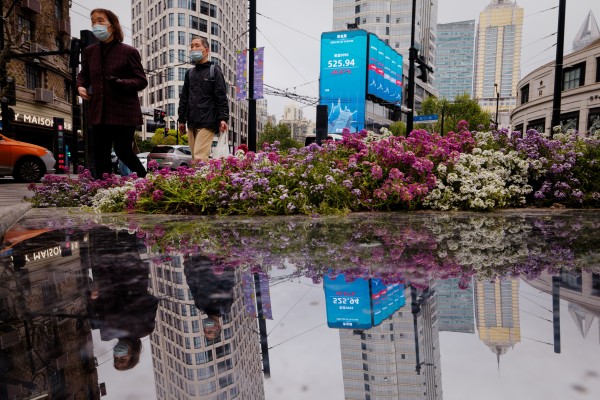 People walk near a screen showing stock exchange and economic data in Shanghai on April 20, 2026. Photo: EPA