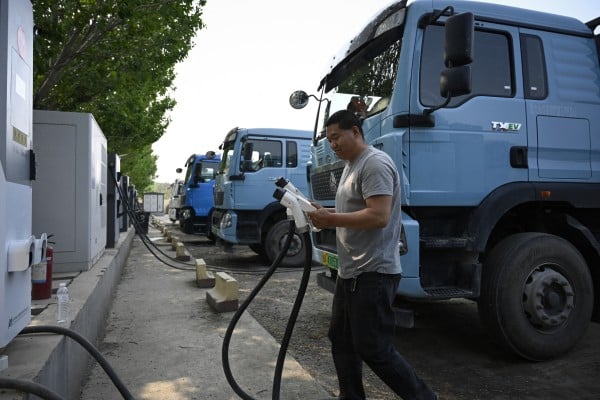 This picture taken on April 23, 2026 shows a driver returning the charging gun after charging his electric truck at a station in Beijing. At a dusty lot an hour outside Beijing, a steady stream of vehicles come and go for a quick battery charge -- just one node in China’s rapidly expanding network of electric trucks. (Photo by WANG Zhao / AFP) / To go with AFP story China-tech-logistics-auto-show, FOCUS by Peter CATTERALL