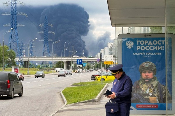 Muscovites go about their daily life as black smoke rises from an oil refinery following a Ukranian drone attack on Thursday. Photo: AFP