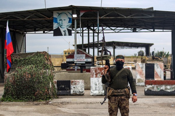 A Syrian rebel fighter stands at an inspection checkpoint for incoming vehicles before a Russian flag and Russian soldiers behind manning the entrance of the Russian-leased Syrian military base of Hmeimim in Latakia province in Syria in 2024. Photo: TNS