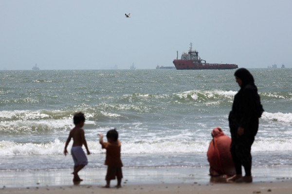 People gather as stranded vessels in the Strait of Hormuz are visible near the beach of Bandar Abbas in Iran on August 25. Photo: Reuters
