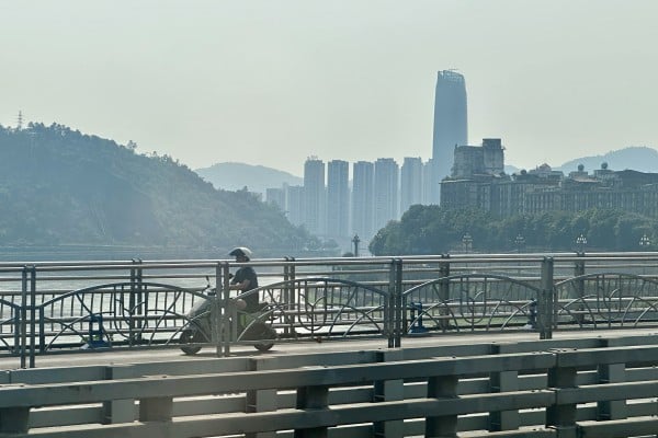 A man rides an electric bike on a bridge that straddles the Yangtze River in Yibin, Sichuan province. Skyscrapers loom against hazy skies in the background. Photo: Frank Chen A man rides an electric bike on a bridge that straddles the Yangtze River in Yibin, Sichuan province. Skyscrapers loom against hazy skies in the background. Photo: Frank Chen