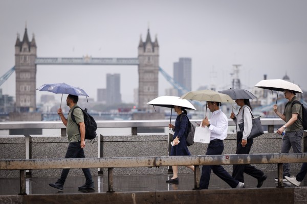 Commuters cross London Bridge during heavy rainfall in Britain on Thursday. Photo: EPA
