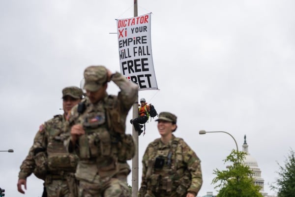 A protester scales a light pole and unfurls a banner to protest the coming state visit by Chinese President Xi Jinping in Washington on Tuesday as members of the National Guard walk by. Photo: AP A protester scales a light pole and unfurls a banner to protest the coming state visit by Chinese President Xi Jinping in Washington on Tuesday as members of the National Guard walk by. Photo: AP
