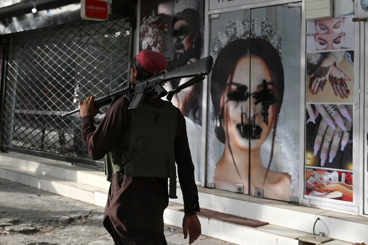 A Taliban fighter walks past a beauty salon with images of women defaced using spray paint in Kabul. Photo: AFP