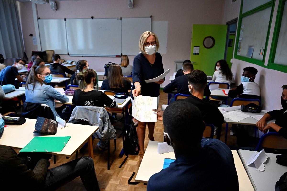 A teacher wearing a protective mask distributes documents to pupils in a classroom in western France. Photo: AFP