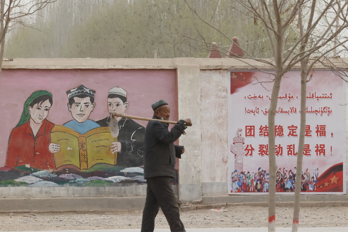 A farmer walks past government propaganda depicting ethnic minority residents reading the constitution with slogans that read, “Unity Stability is fortune, Separatism and Turmoil is misfortune,” near Kashgar in northwestern China’s Xinjiang Uyghur Autonomous Region in March 2021. Photo: AP