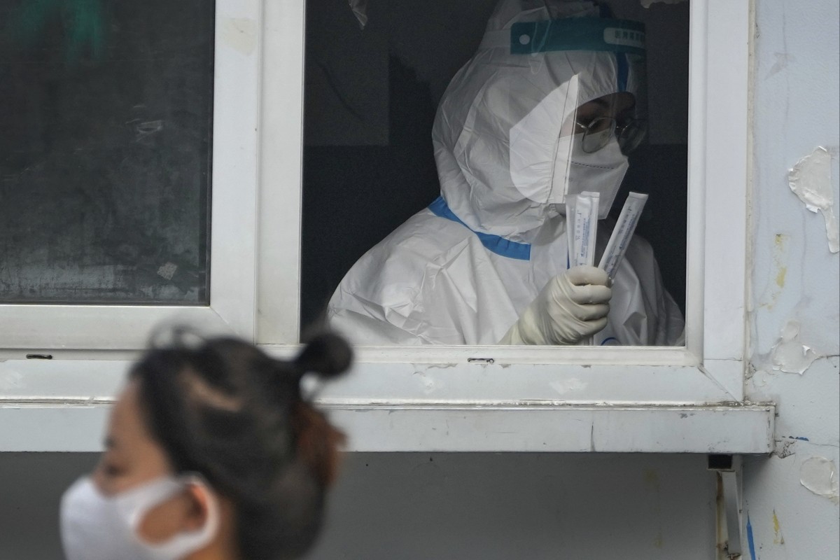 A woman wearing a face mask walks by a medical worker preparing to administer Covid-19 tests at a coronavirus testing site in Beijing. Photo: AP