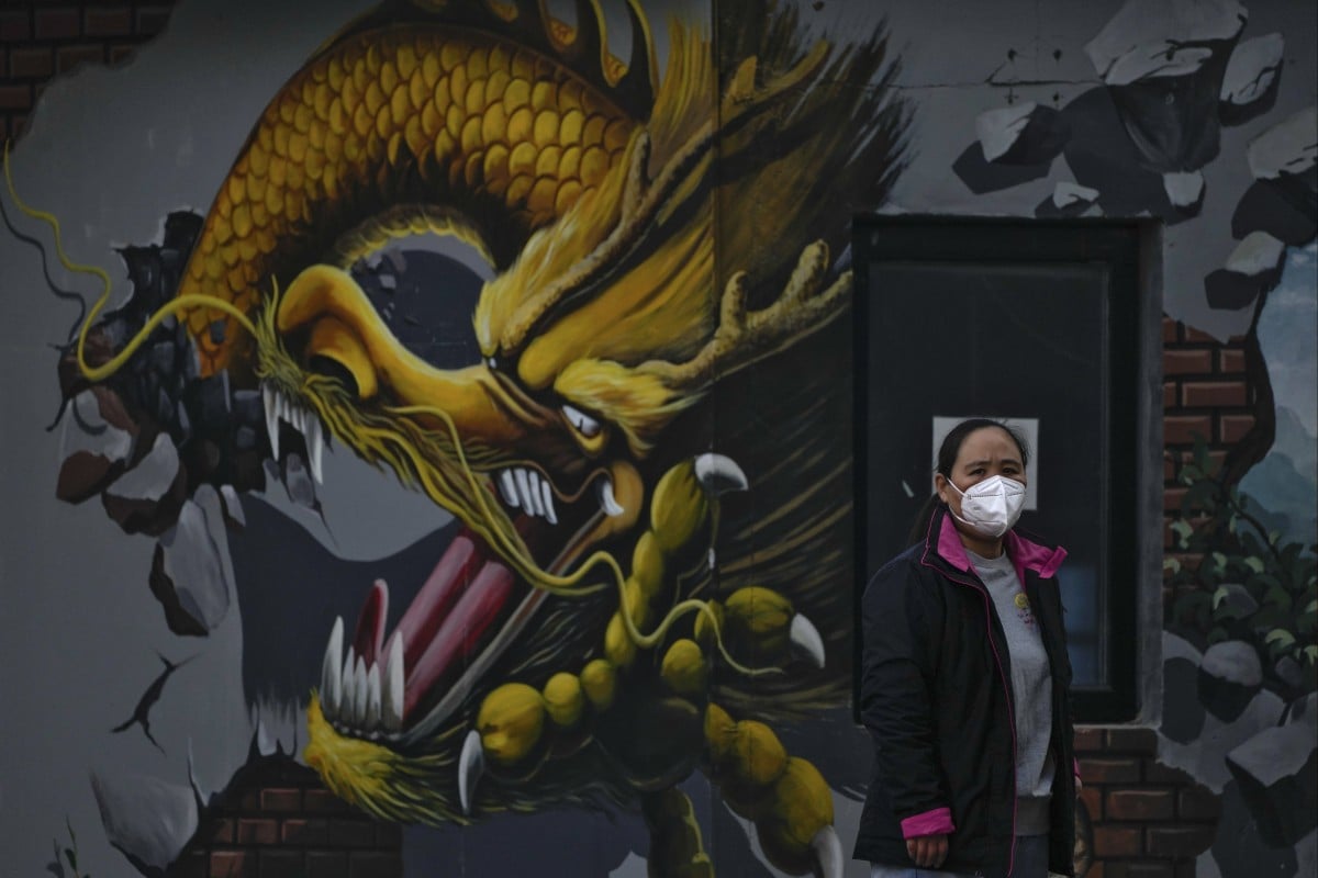 A woman wearing a face mask stands near a mural depicting a dragon in Beijing on Wednesday, November 23, 2022. China is seeing its highest number of coronavirus cases since the pandemic began. Photo: AP