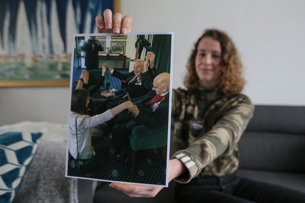 In this photo taken on Tuesday May 5 2020, Marion Nivard, 15, a student at Saint-Louis Middle School in Cabourg, shows a photo of WWII veterans, including Bill Ridgewell, in Varaville, Normandy.As V-E Day approached, Nivard and her classmates in the Normandy region thought of 94-year-old Bill Ridgewell and other vets living in isolation because of the COVID-19 pandemic — just as they were. The teens decided to swap stories with the men about their lives under lockdown. (AP Photo/David Vincent)