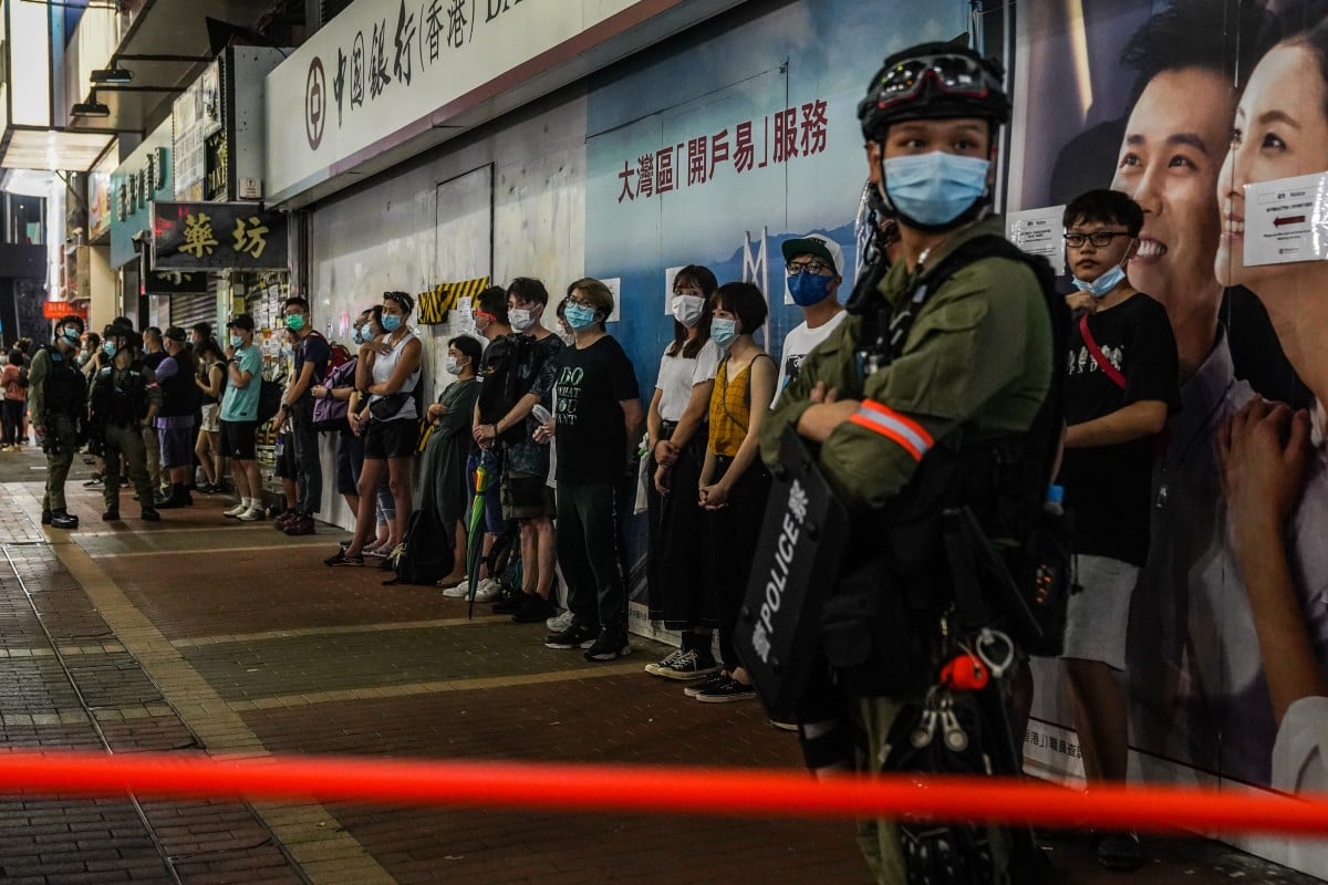 People stand in line wearing protective face masks as they are stopped and searched by riot police during a protest in Hong Kong. Photo: Bloomberg