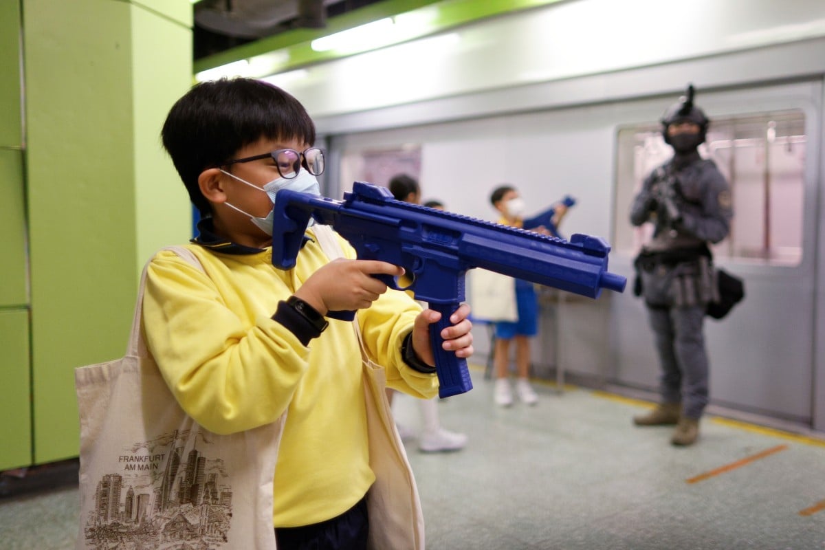 Children play with toy guns next to a member of the Railway Response Team at a model of an MTR station. Students visited the Hong Kong Police College during an open day to mark National Security Education Day. Photo: Reuters