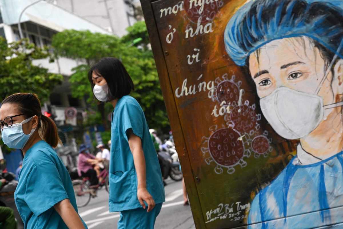Nurses wearing face masks walk past an electricity box decorated with a coronavirus-themed painting on a street in Hanoi. Photo: AFP