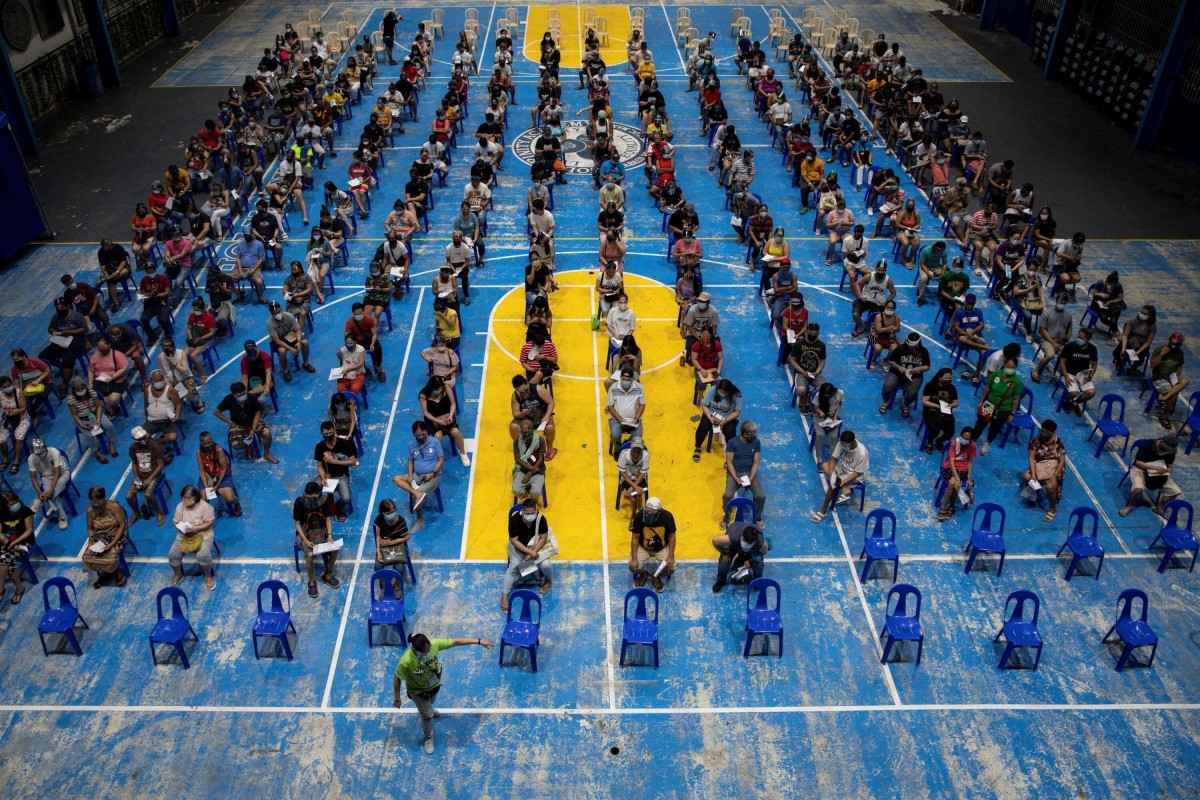 A government worker assists people queueing to get the Moderna Covid-19 vaccine at a school turned into a 24/7 vaccination site in Manila, Philippines. Photo: Reuters