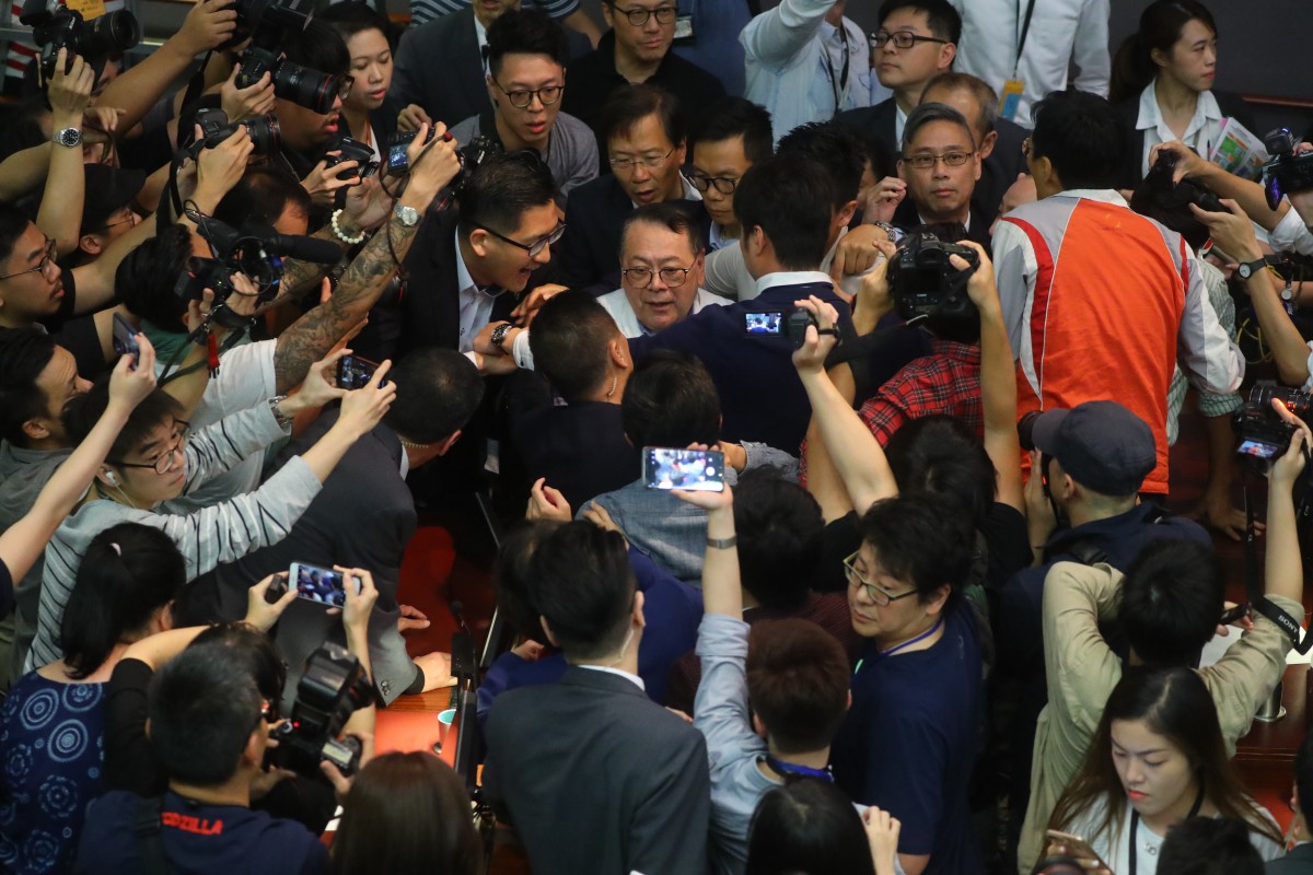 Legislator Abraham Razack is surrounded by lawmakers and the media in chaotic scenes inside the Legislative Council.