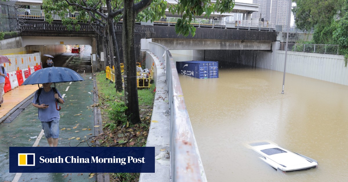 A person walks with an umbrella along a flooded street under a bridge, while a car appears to be partially submerged in muddy floodwaters following a black rainstorm in Hong Kong, 2025.