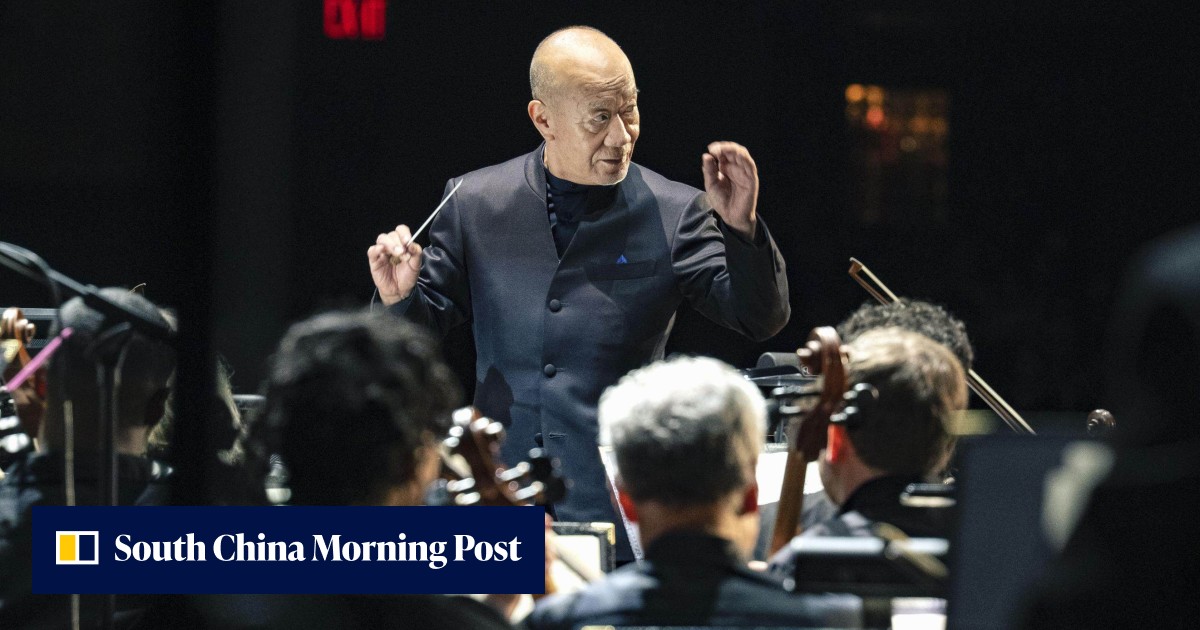 Joe Hisaishi conducting an orchestra on stage with projected film scenes behind him