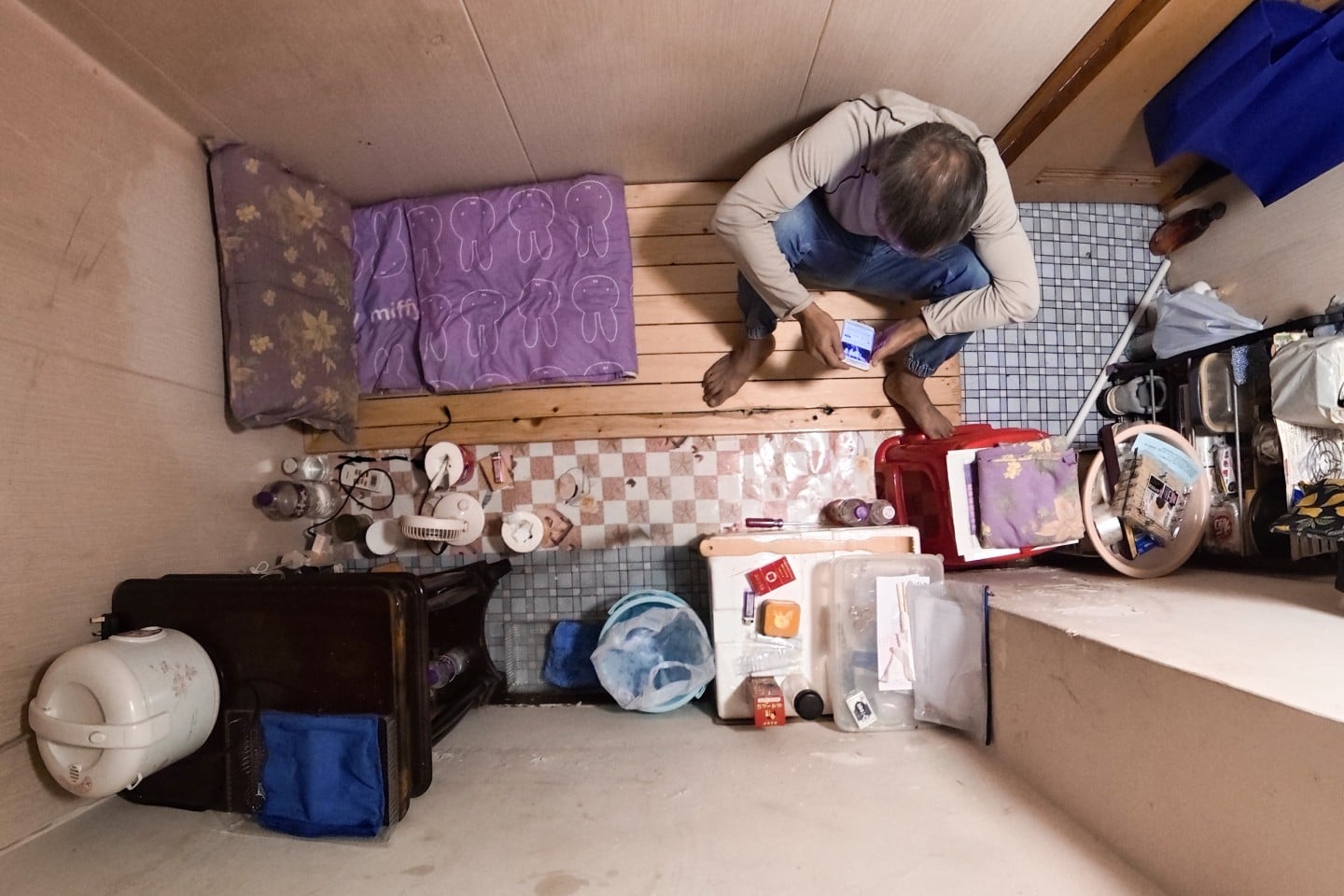 A tenant uses his phone inside his cubicle home in Sham Shui Po on October 23. Photo: Eugene Lee