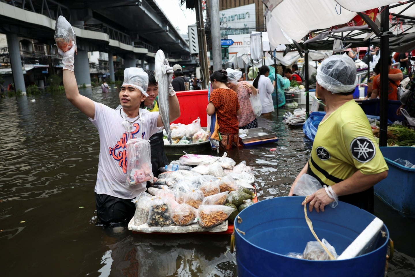 A fish vendor, with his supplies for sale on a floating platform, holds up fish as people navigate through a flooded market, in Bangkok, Thailand, September 28, 2026. Photo: Reuters