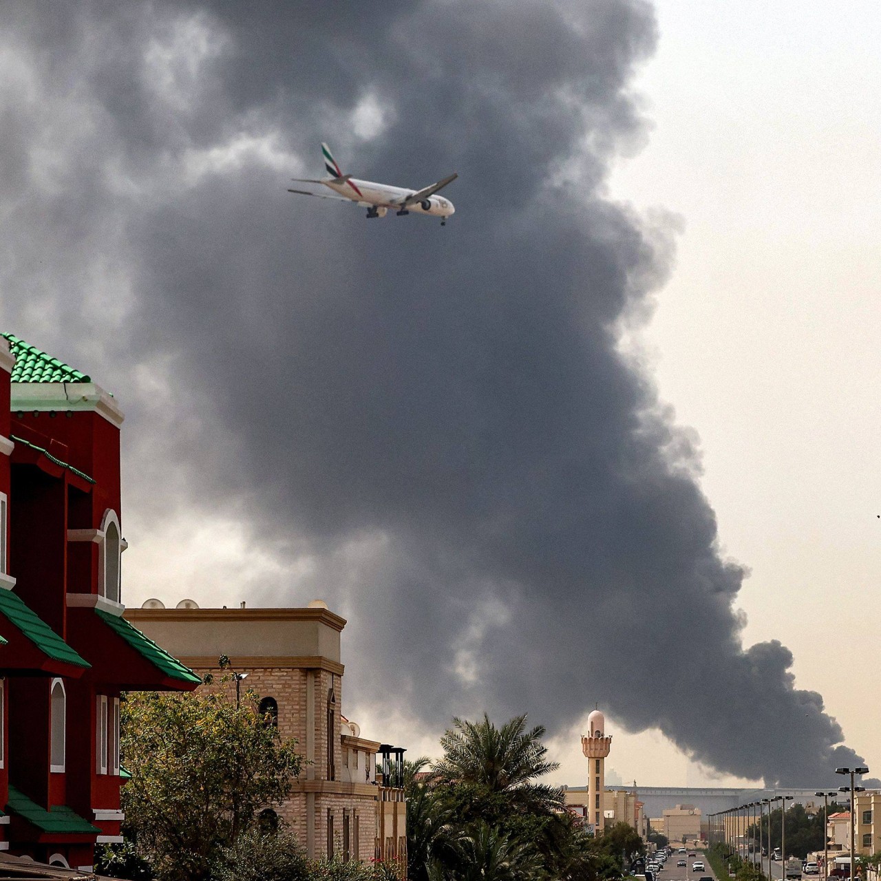 An Emirates aircraft prepares for landing as a smoke plume rises from a fire near Dubai International Airport on March 16. Photo: AFP