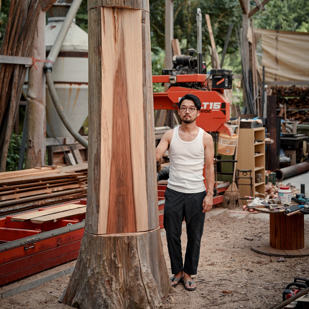 Shinya Kobayashi beside a cedar, the wood he uses as much as possible 
in the construction of his “village”. Photo: courtesy Mujun 